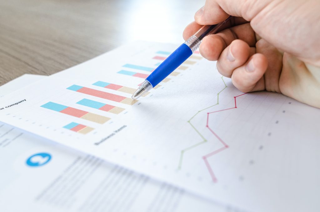 A hand holding a pen on a piece of printed paper depicting bar charts.